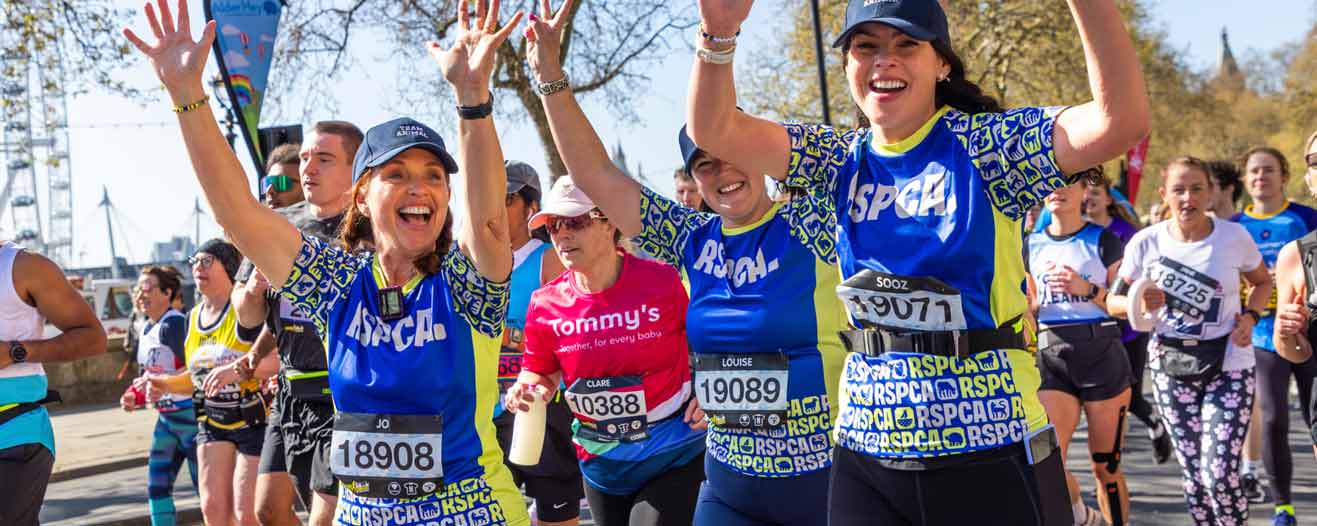 Three women in RSPCA running shirts smile and wave while taking part in the London Landmarks Half Marathon.